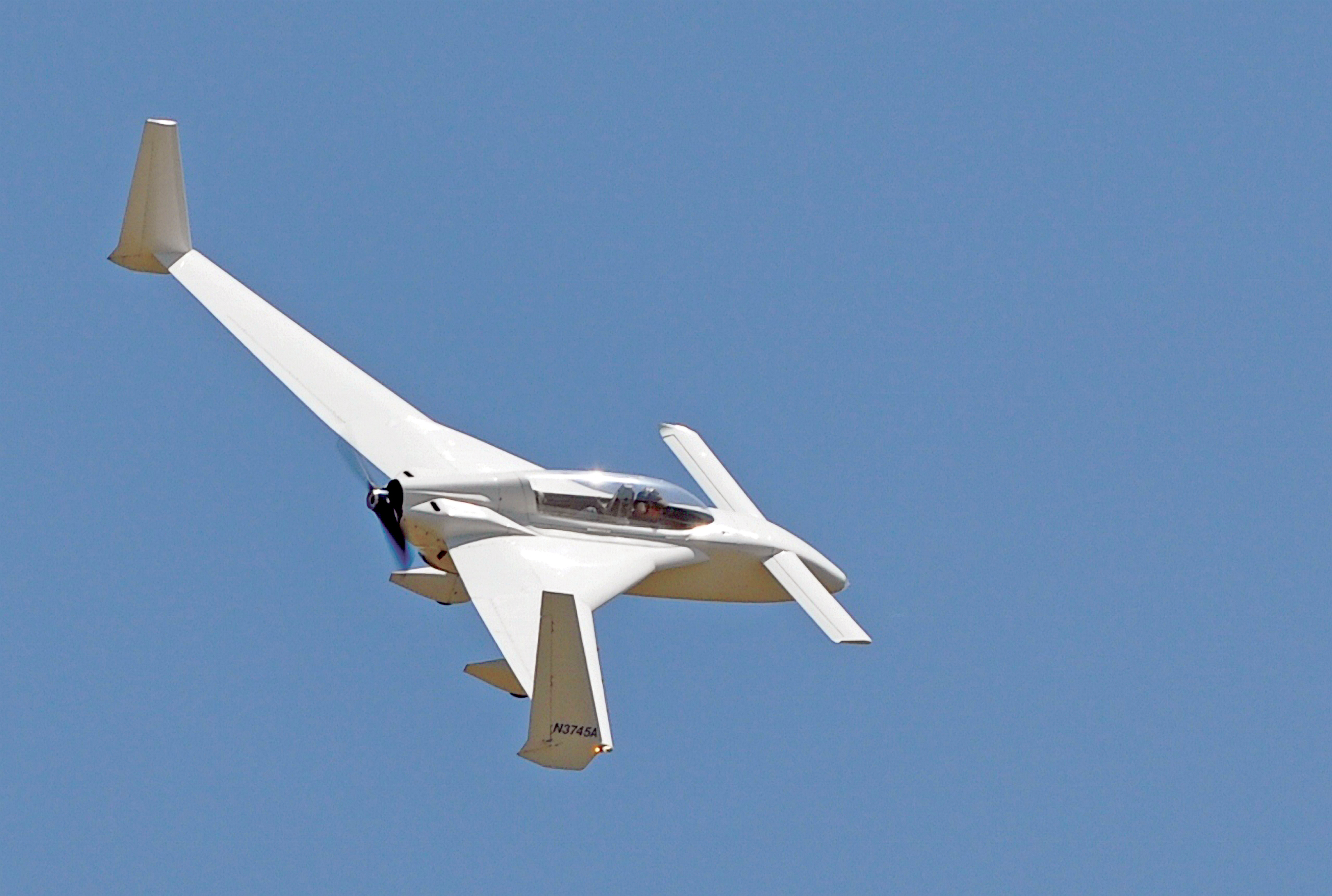 White aircraft with a unique wing design flying in a clear blue sky.