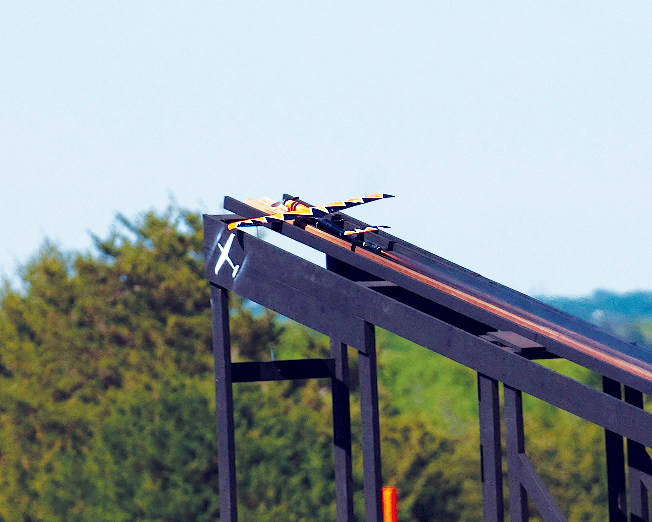 Large wooden structure with slanted beams against trees and sky.