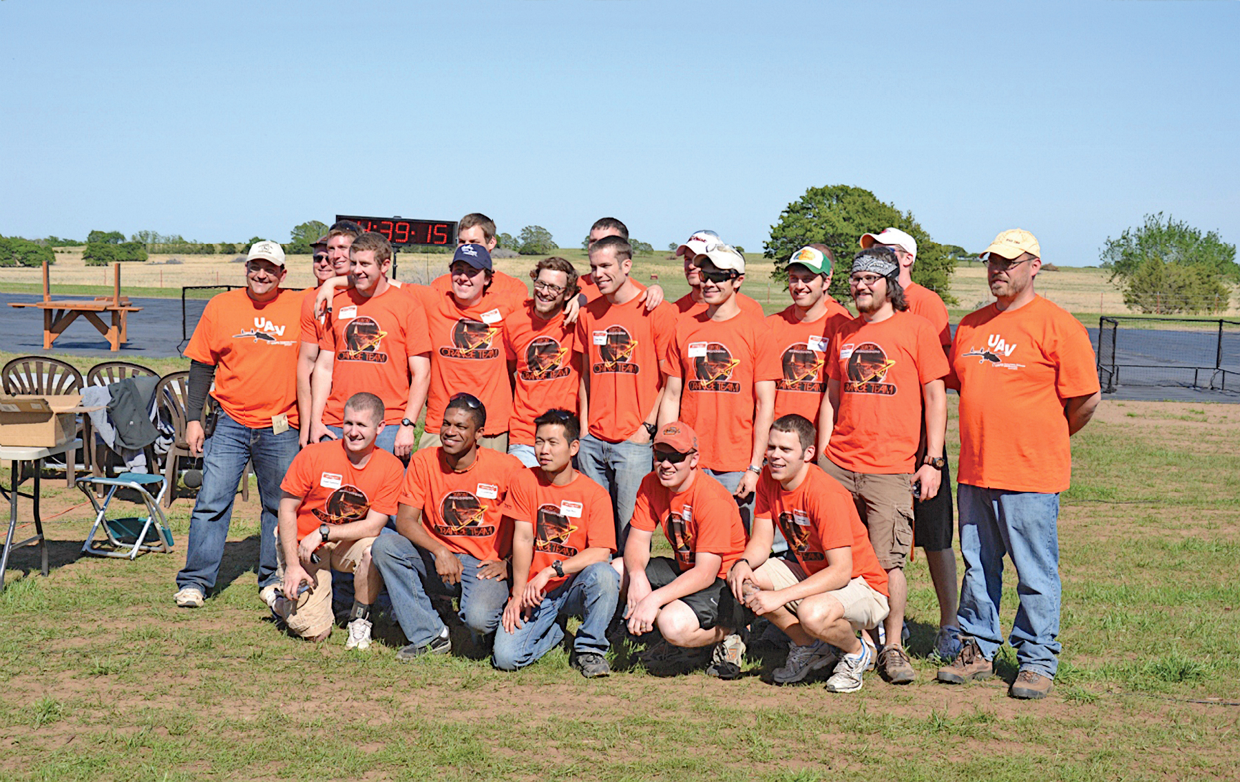 A group of people in orange shirts posing outdoors on a sunny day.