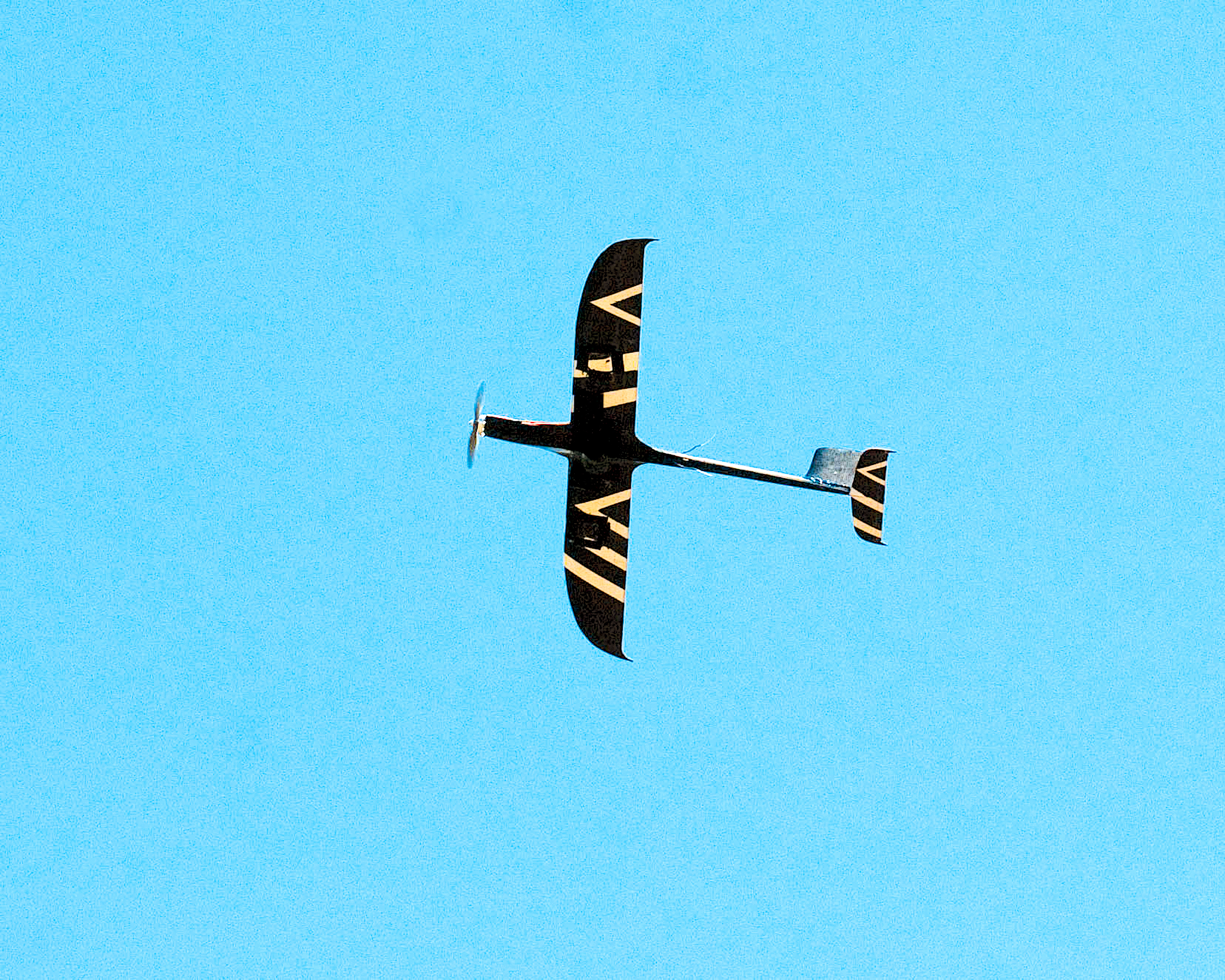 Aircraft with geometric patterns on wings, flying in clear blue sky.