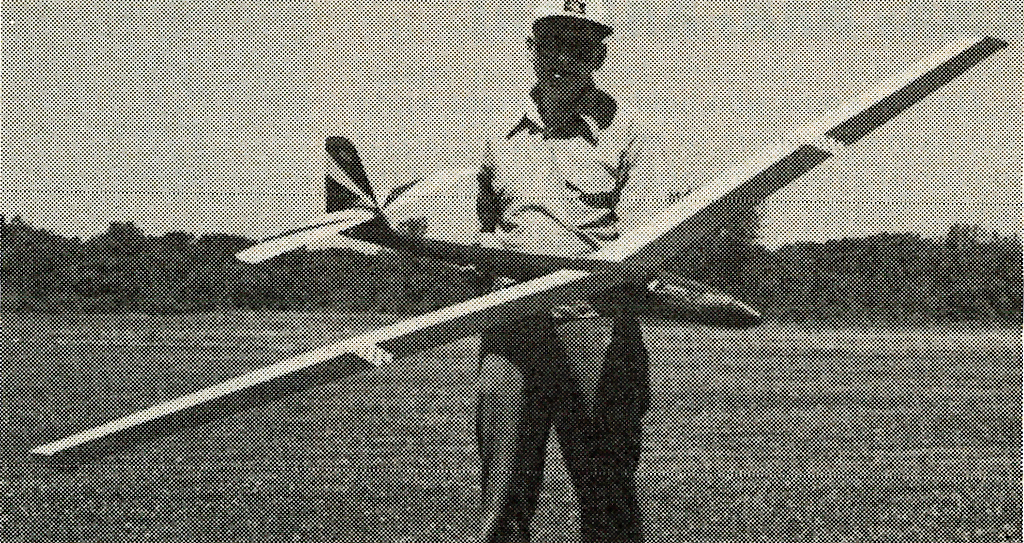 Man holding a large model glider on a grassy field.