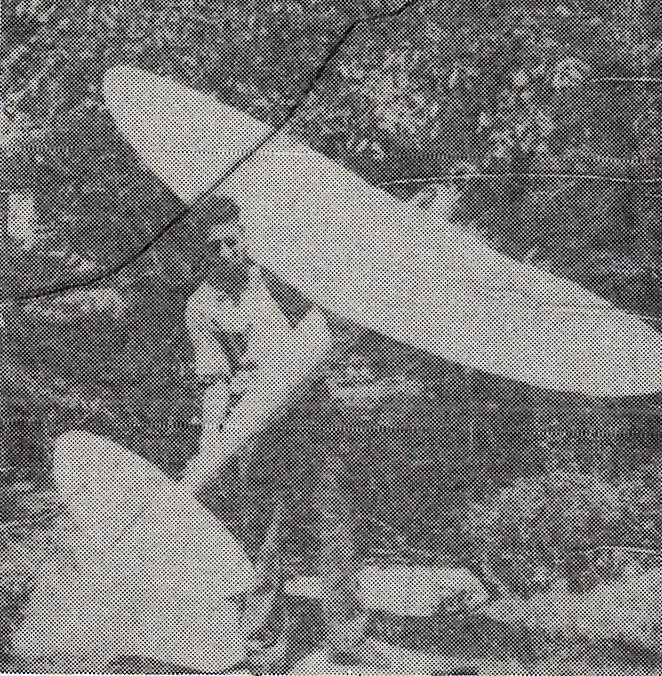 Black and white photo of a man holding a large model glider outdoors.