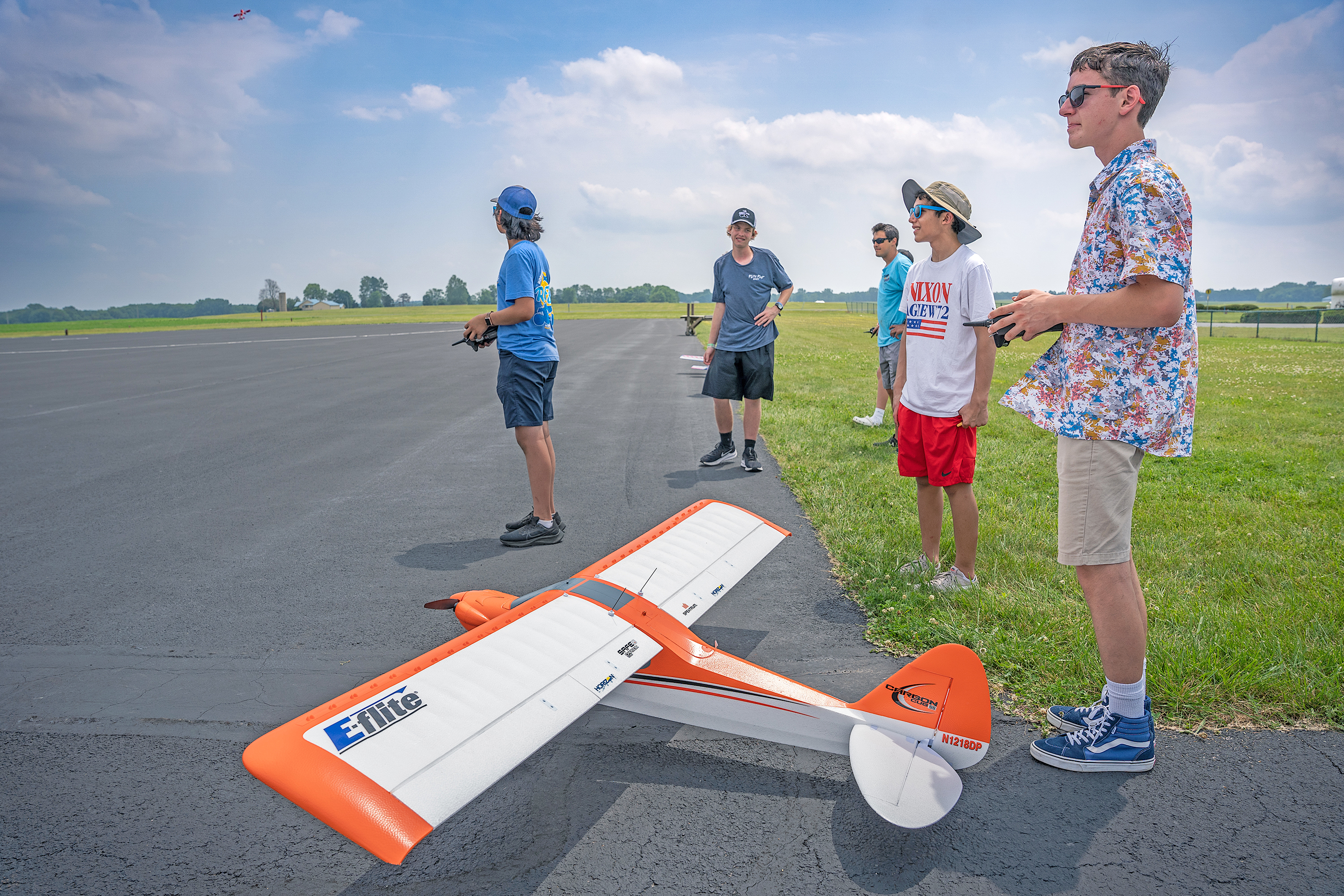 Remote-controlled airplane on runway with five people watching.
