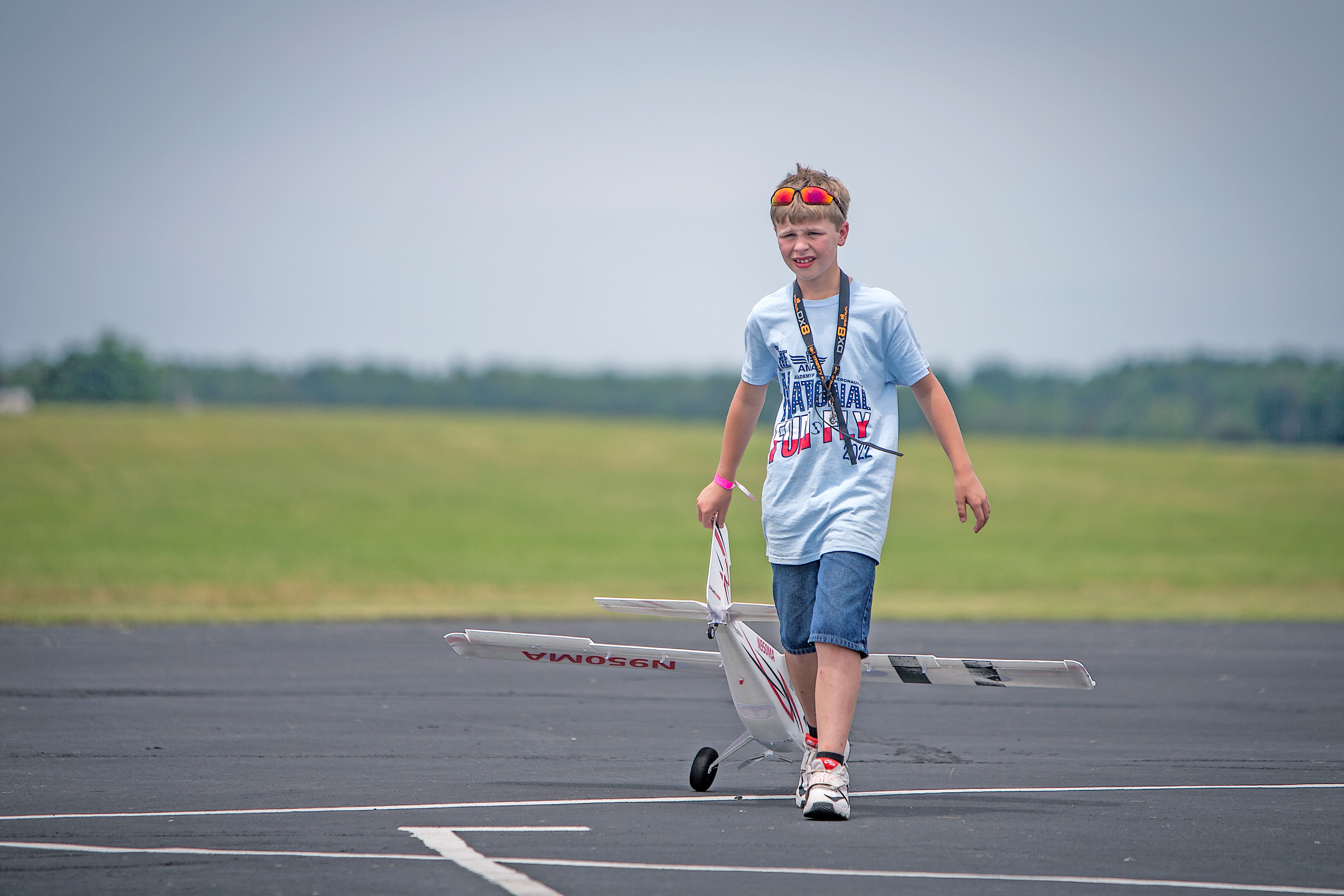 Boy walks on runway holding RC plane, wearing a blue shirt and headband.