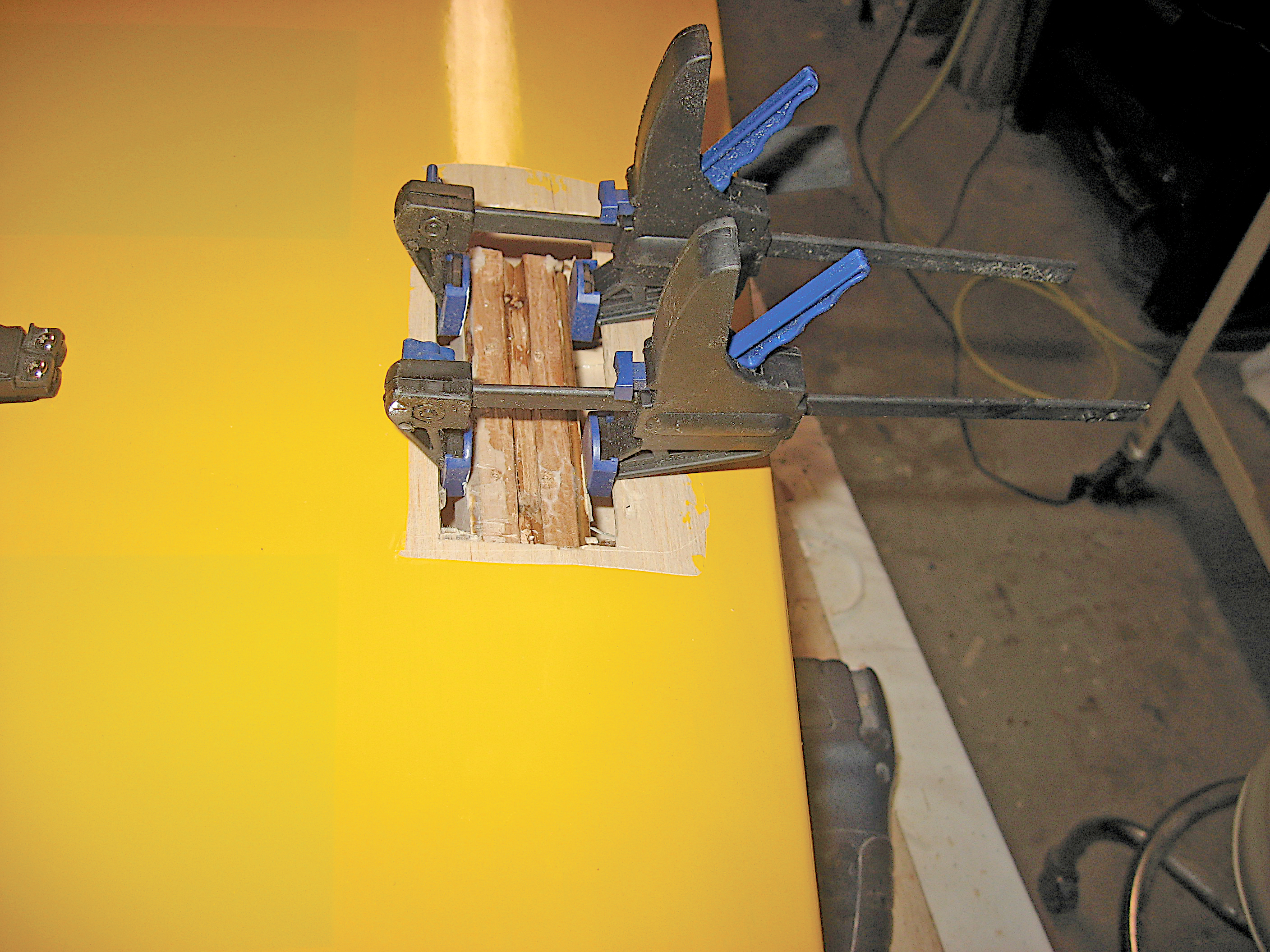 Wood clamped on yellow tabletop with blue and black clamps.