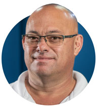 Bald man with glasses, smiling in front of a blue background.