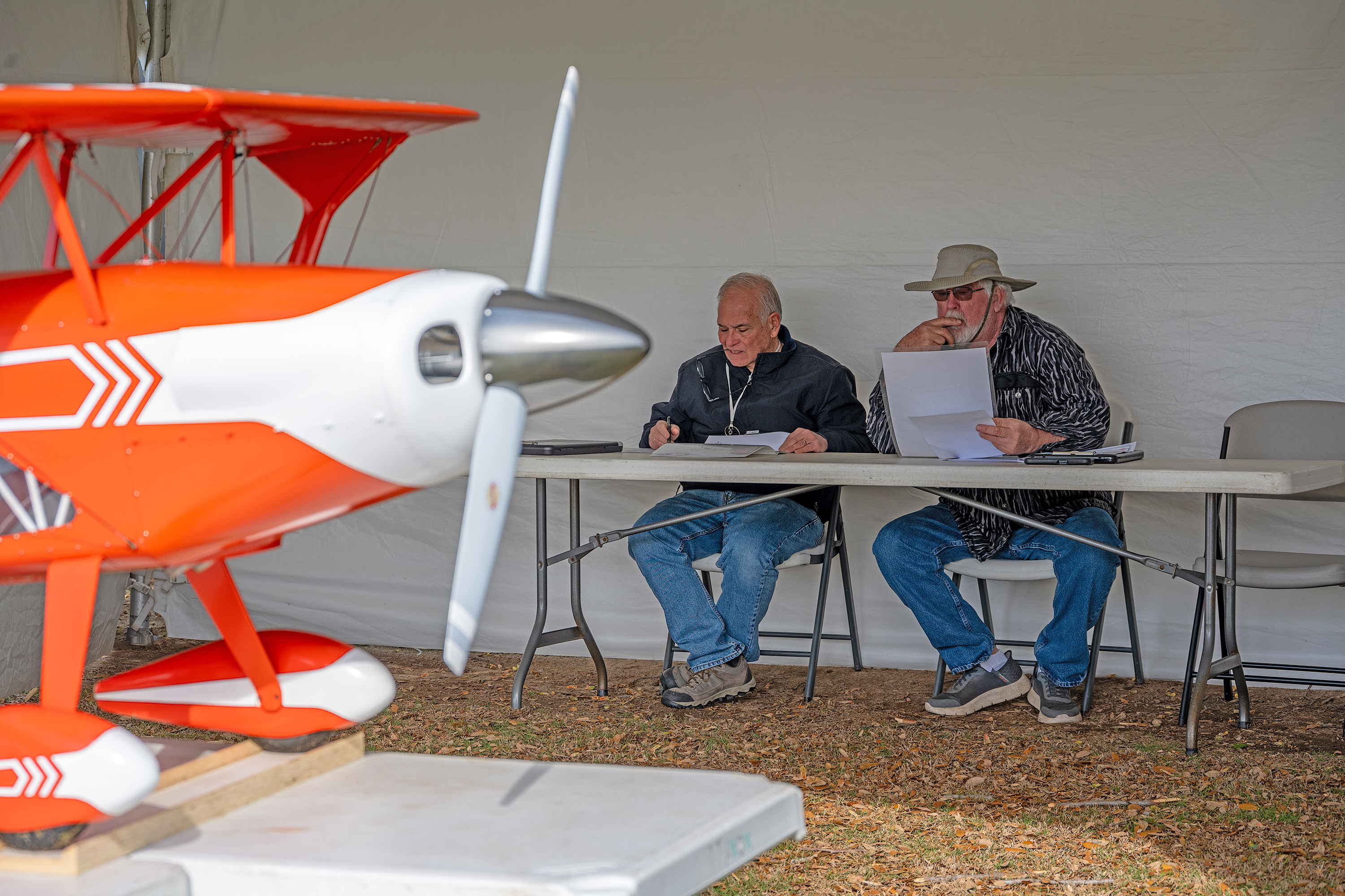 Orange and white model plane with two seated men evaluating it.