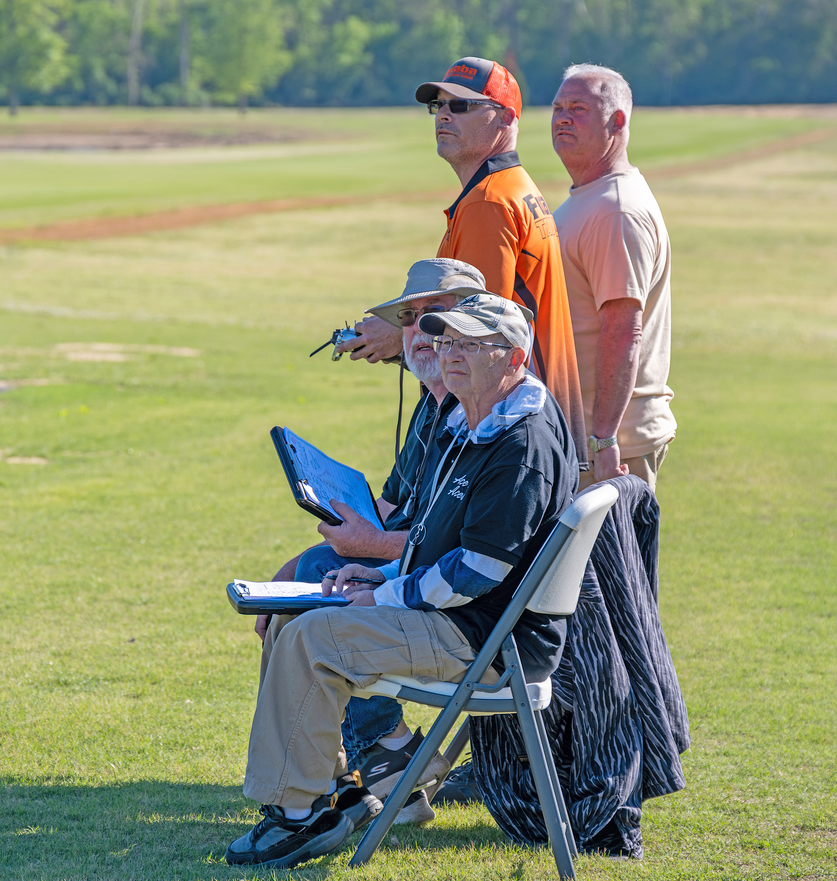 Two men standing, two seated in a grassy field under a clear sky.