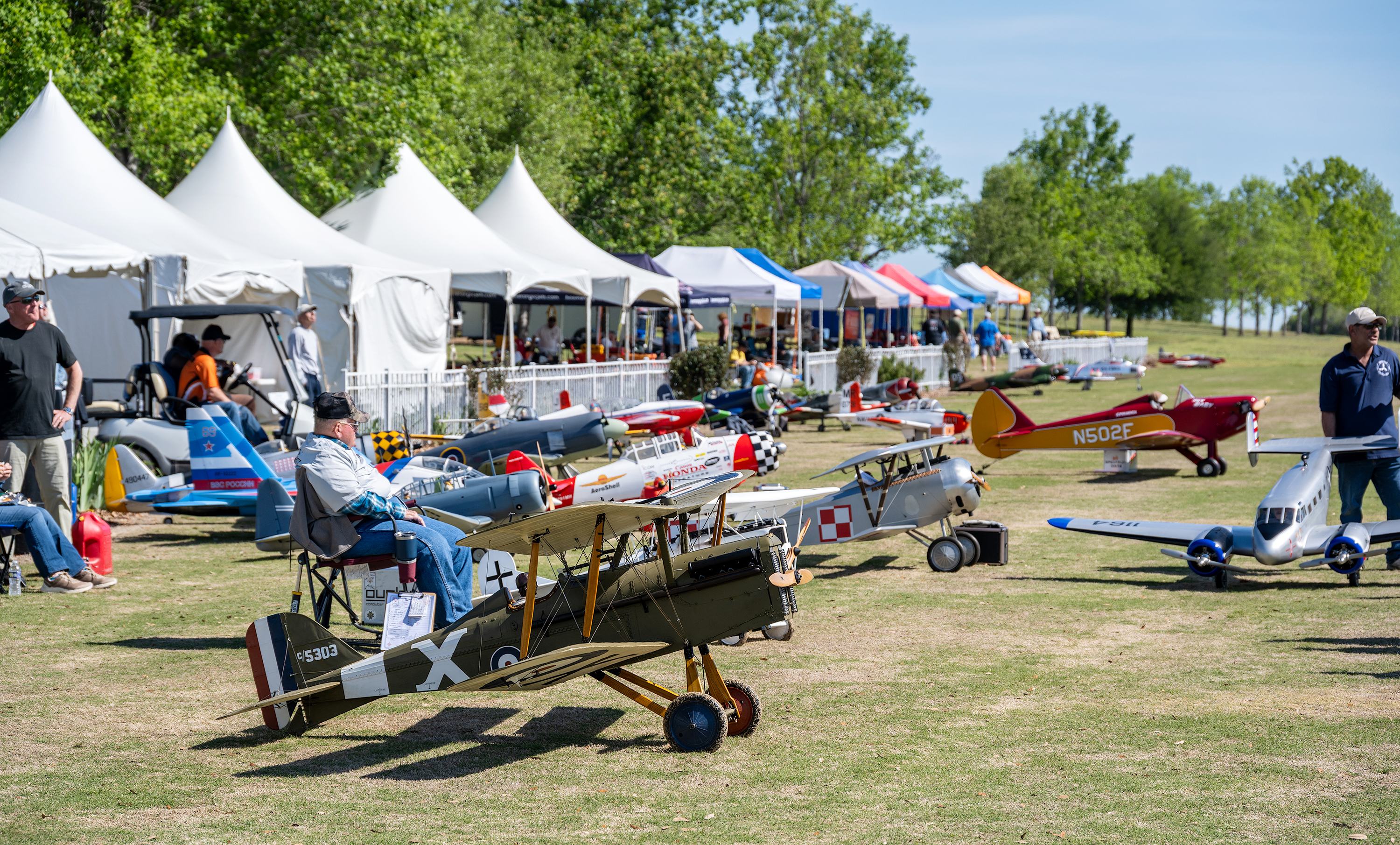 Model airplanes displayed at an outdoor event with tents and spectators.