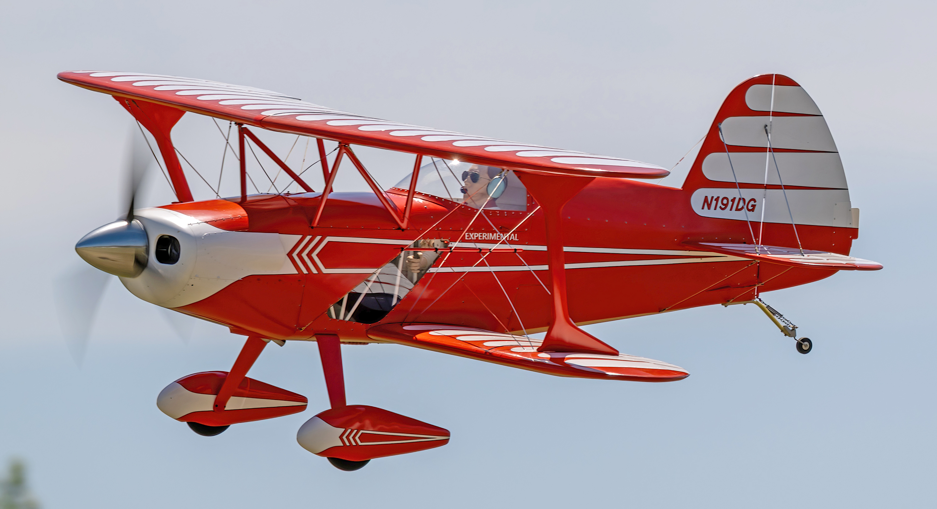 Red and white biplane in flight against a blue sky.