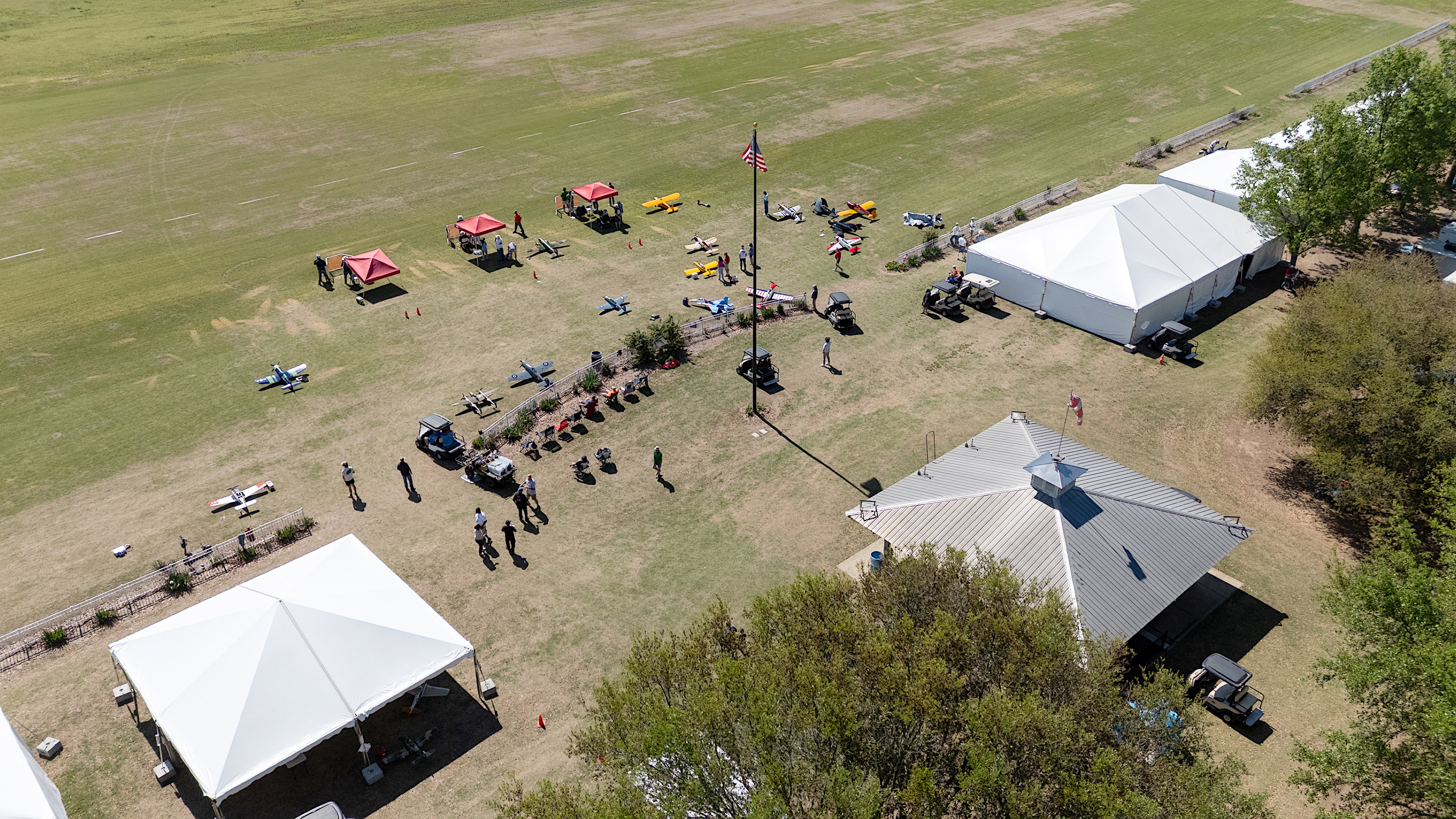 Aerial view of a field with white tents, people, and tables.