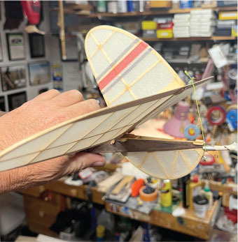 Hand holds a wooden model airplane with striped wings in a cluttered workshop.