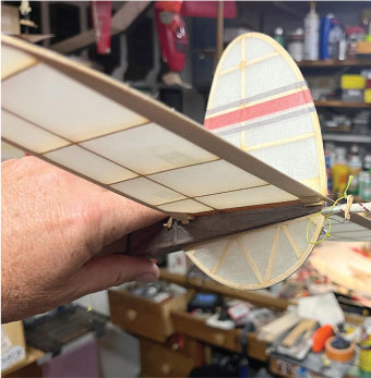 Model airplane with a hand holding the tail, in a cluttered workshop.