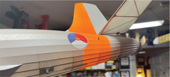 Orange and white model airplane tail with roundel, indoor setting.