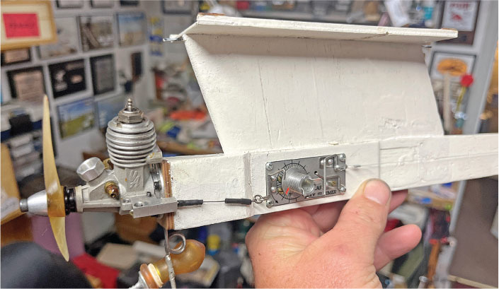 Hand holding a model airplane wing with a small engine in a cluttered room.