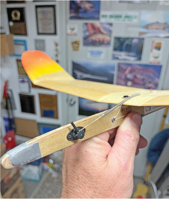 Hand holding a wooden model airplane with an orange and yellow tail.