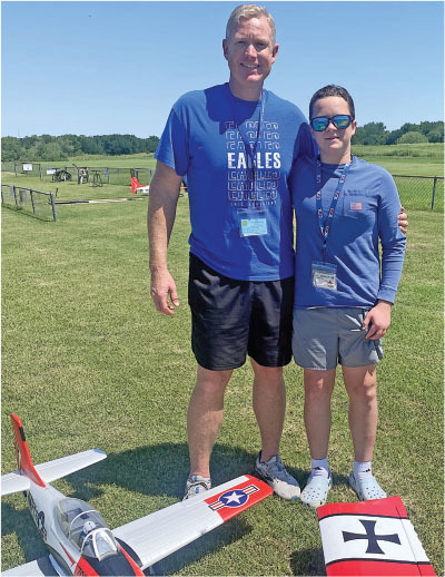 Two people smiling with a model plane on grass.