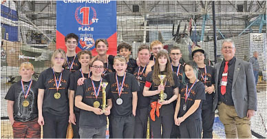 Group of teens and a man with medals, trophies, and "1st Place" banner.