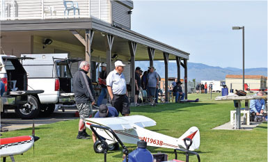 Men gathered near a small, white model airplane outside a building.