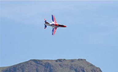 Jet with red, white, and blue design flying over a mountain against a clear sky.