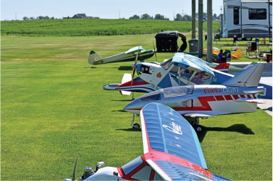 Model airplanes lined up on a grassy field with a camper nearby.