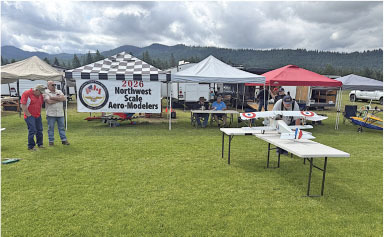 Outdoor model airplane event with tents and spectators on a grassy field.
