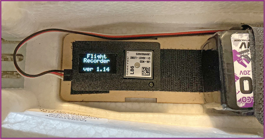 Electronic device with a small display showing text, connected to a battery.