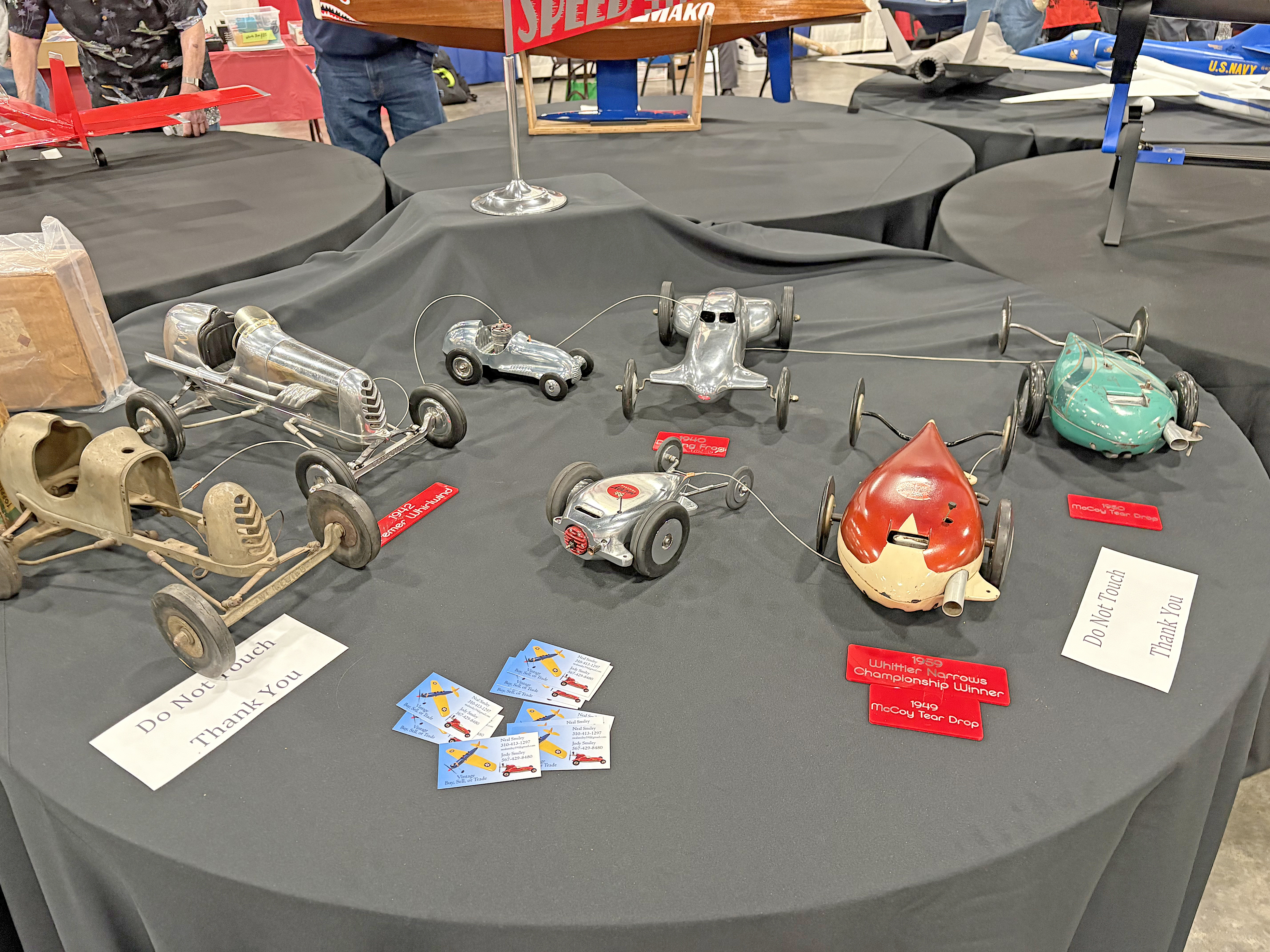 Toy cars displayed on a black-covered table with small labels and postcards.