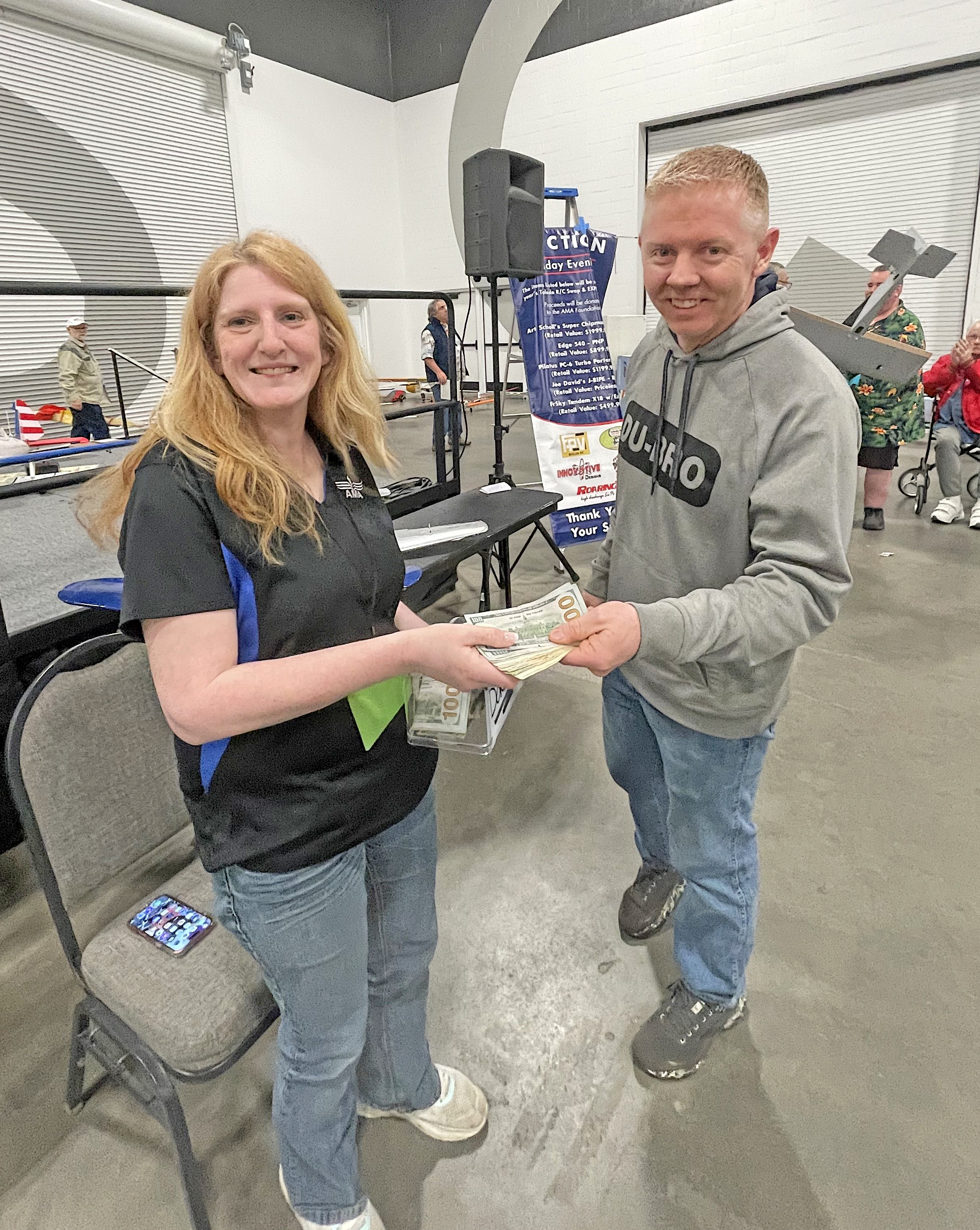 Man and woman smiling, holding a stack of dollar bills indoors.