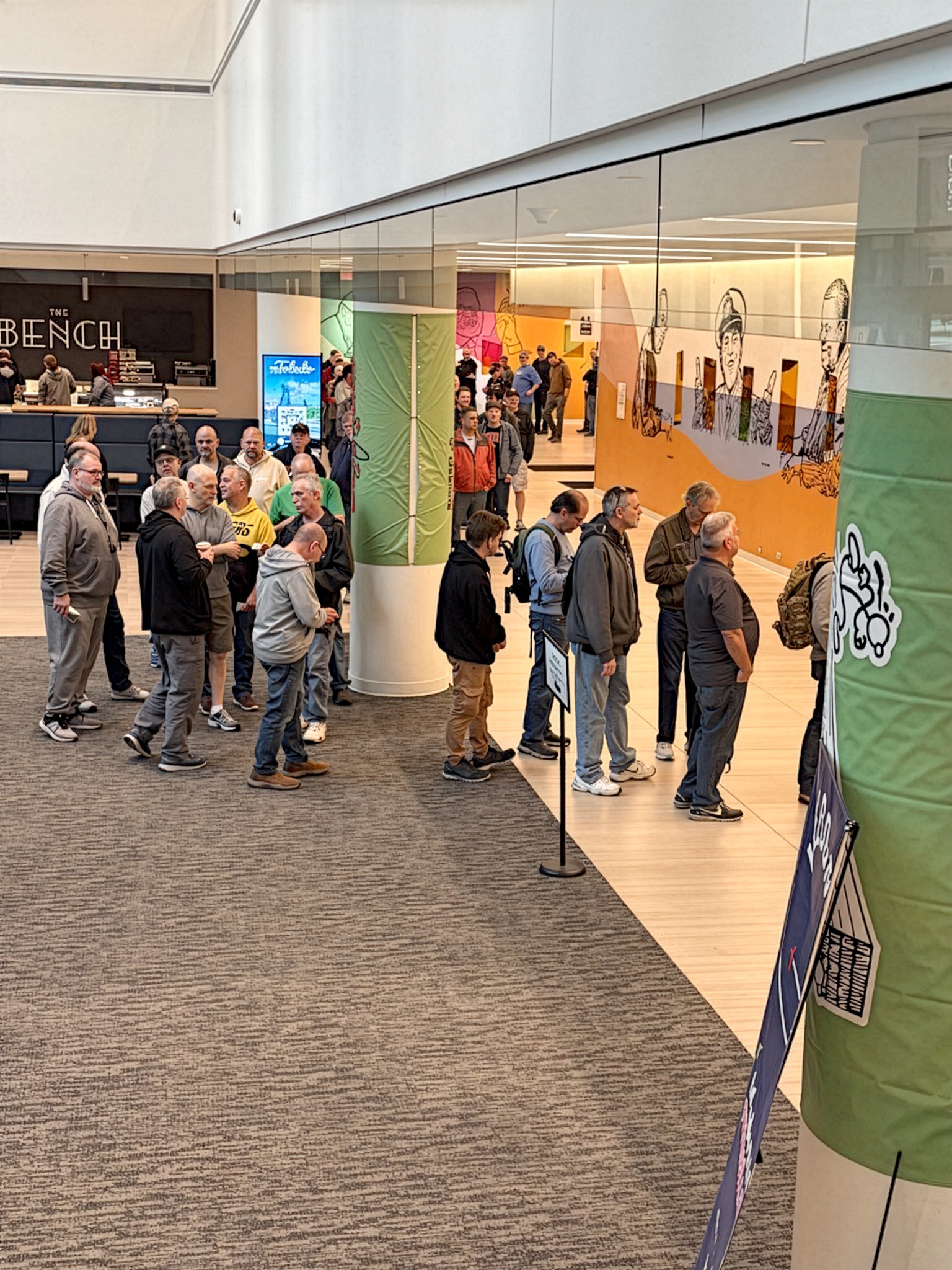 Queue of people in a hallway near a colorful exhibition.