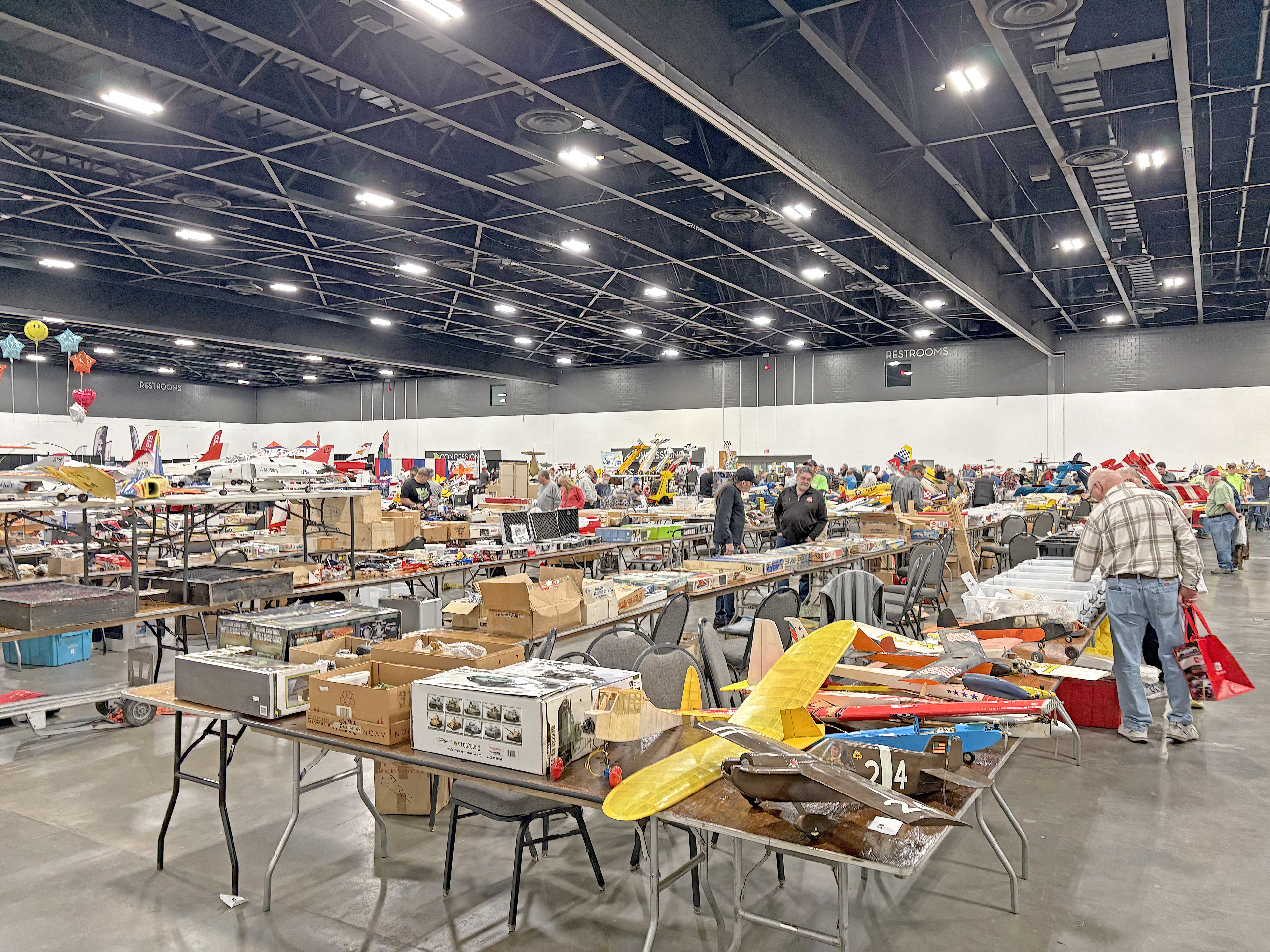 Busy convention hall with model airplanes on tables.