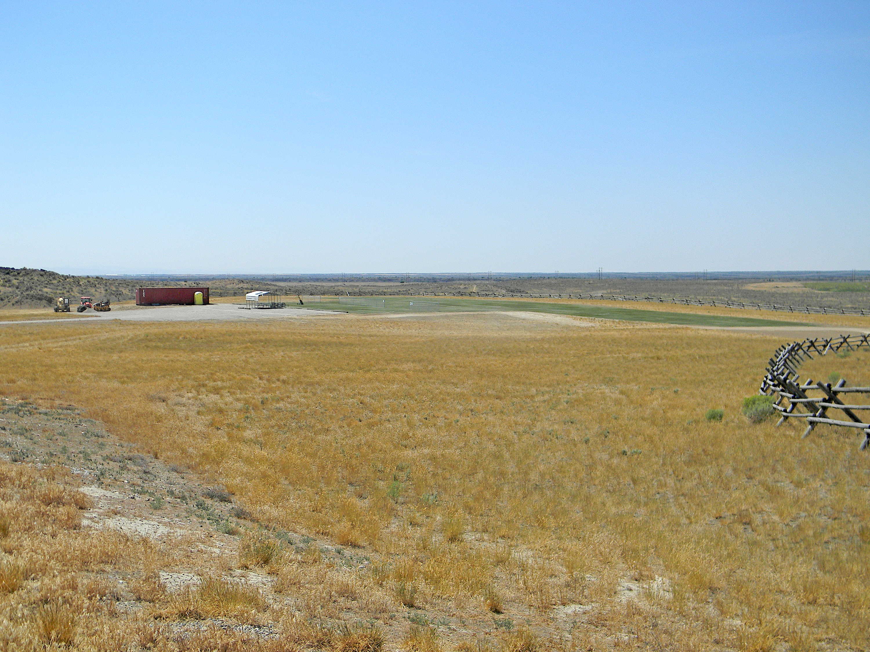 Dry grassy field with distant buildings under a clear blue sky.