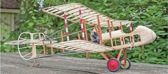 Wooden toy biplane with red wheels on a table, greenery in the background.