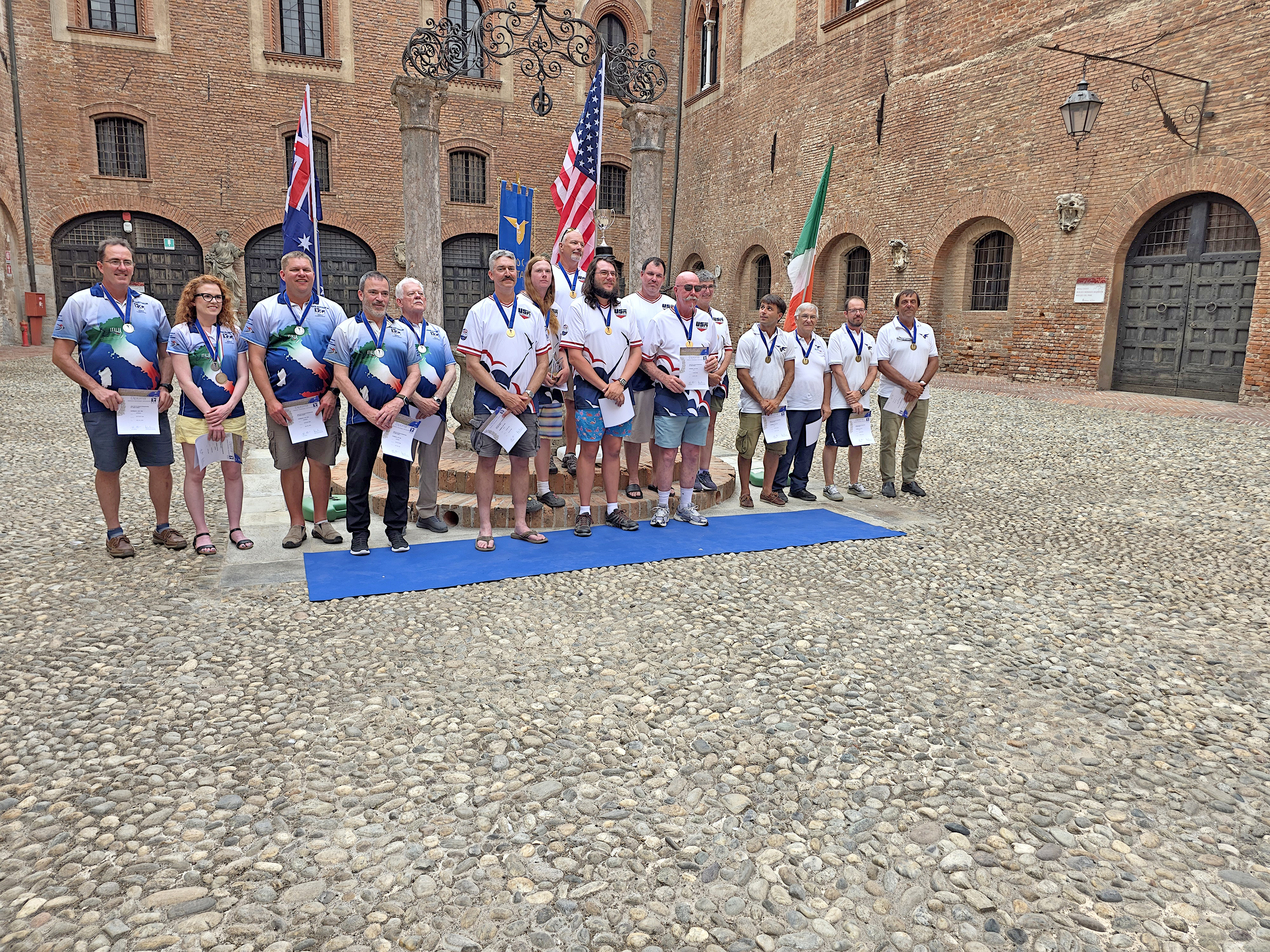 Group of people in sports attire standing on a blue mat in a cobblestone courtyard.