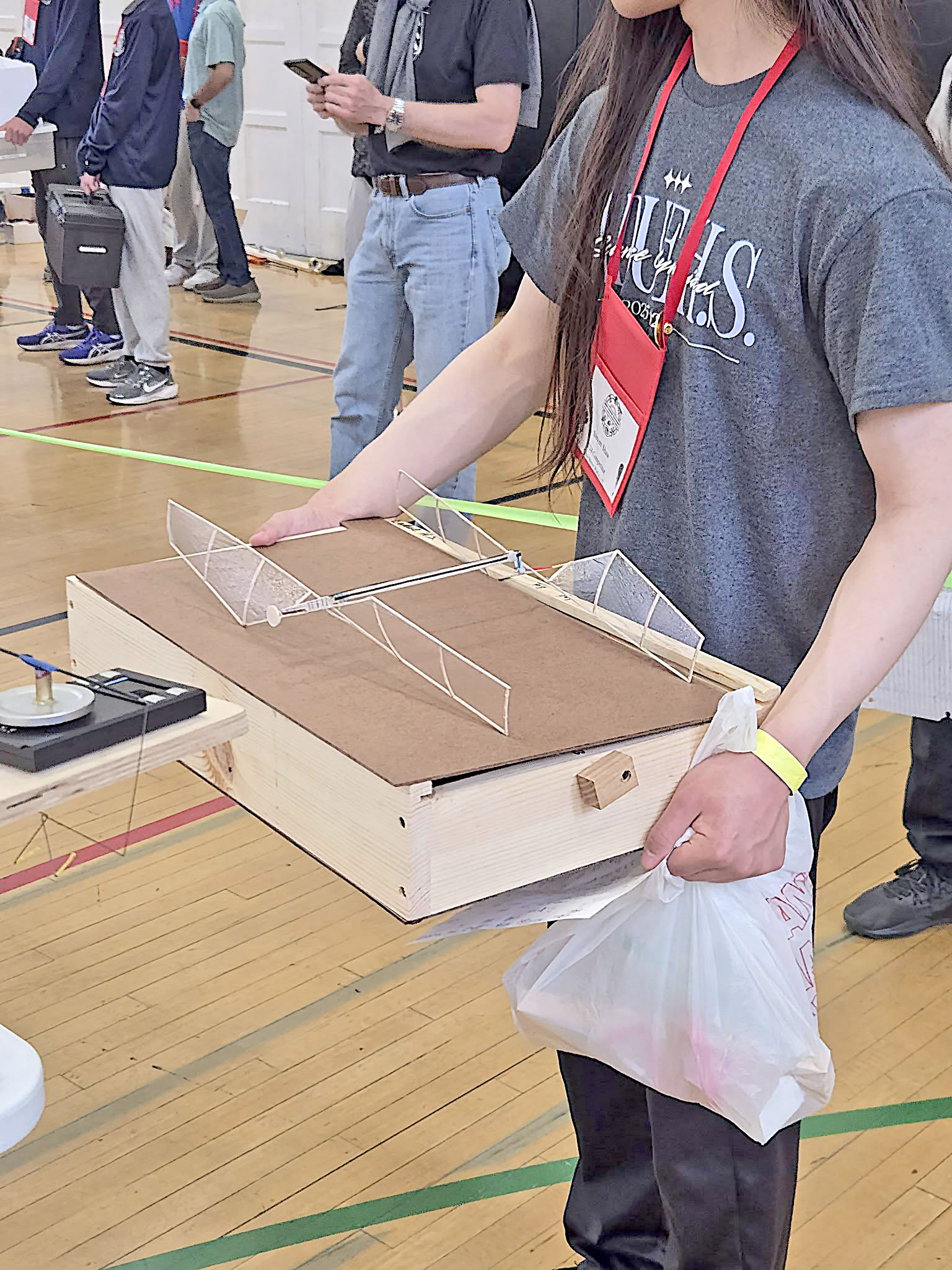 Person holding a wooden craft in a gym with standing people around.