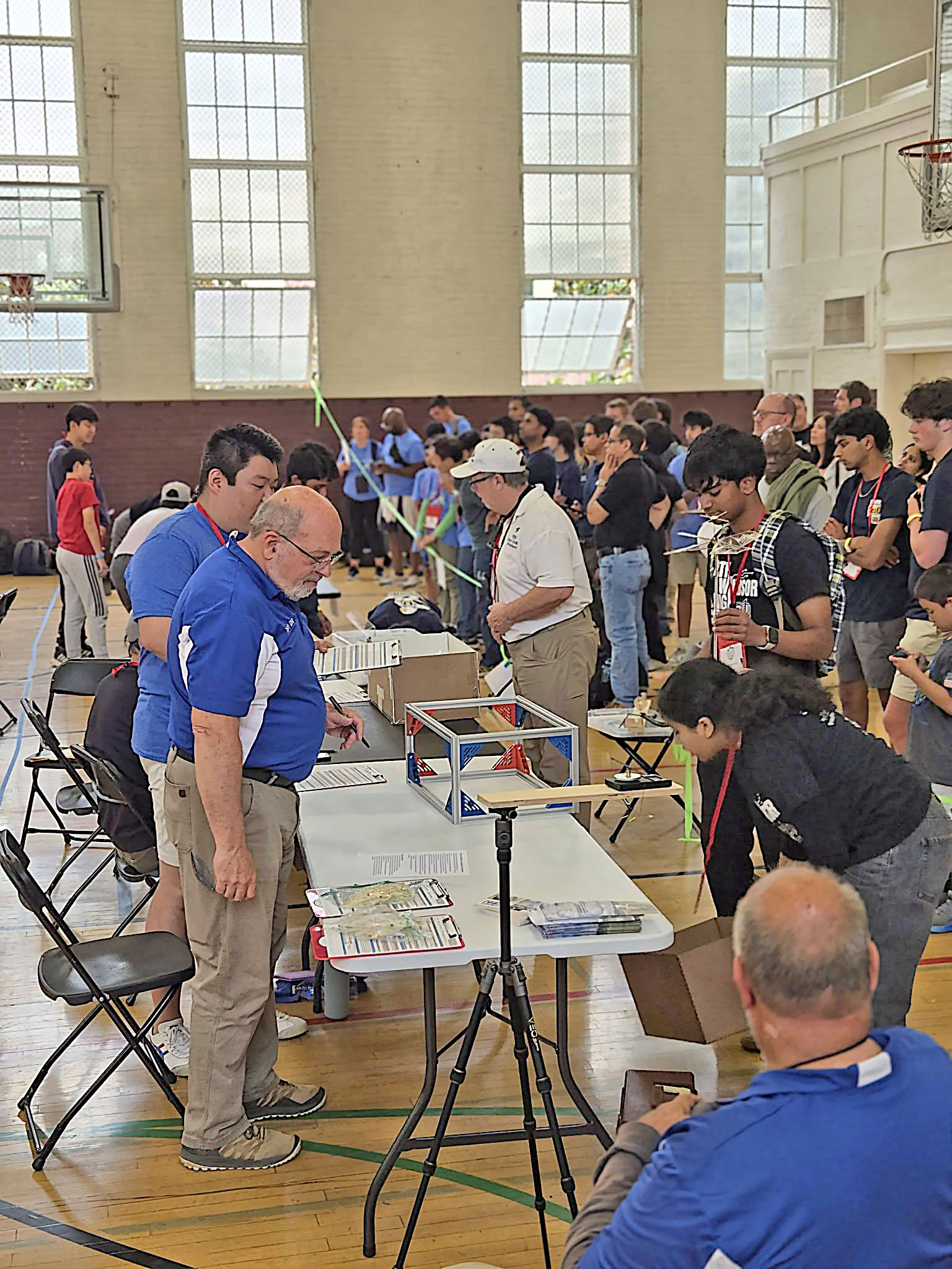 People gathered around tables in a gymnasium for a robotics event.