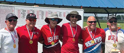 Six men smiling, wearing medals and "USA" shirts, standing under a pavilion.