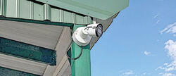 Security camera mounted on a green building under a blue sky.