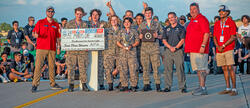 Group of people celebrating with a large check and trophy outdoors.