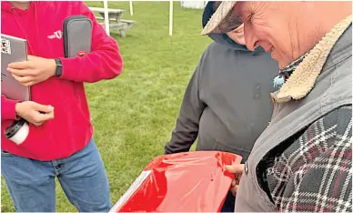 Three people outdoors examining a red tray or object, grass in the background.