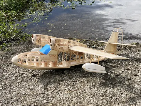 Wooden model seaplane on gravel by the water.