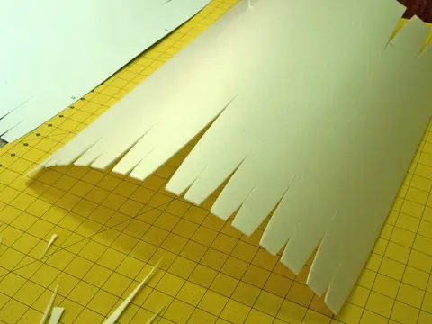 Curved paper with fringes on a yellow cutting mat.