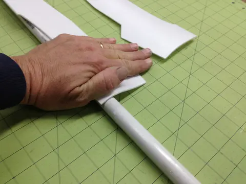 Hand pressing foam onto a white tube on a green grid cutting mat.