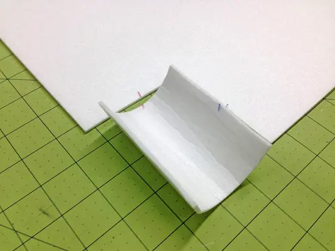 Folded white paper on green gridded cutting mat.