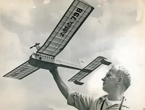 Man holding a model airplane labeled "N-798" against a cloudy sky.