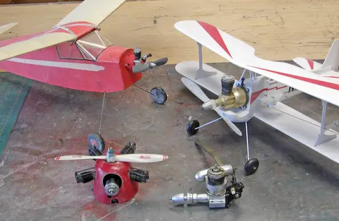 Red and white model planes with their engines on a workbench.