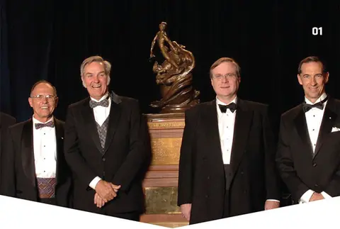 Five men in tuxedos stand in front of a bronze statue.