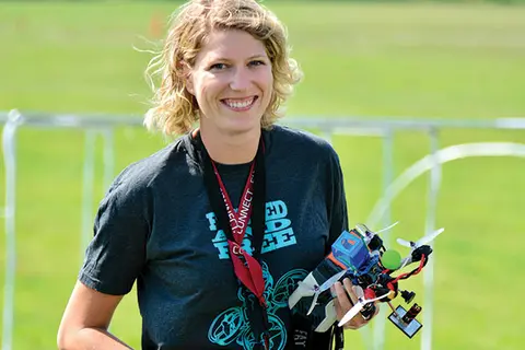 Smiling woman holding a small drone outdoors.