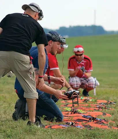 People kneeling on grass, setting up drones with controllers.
