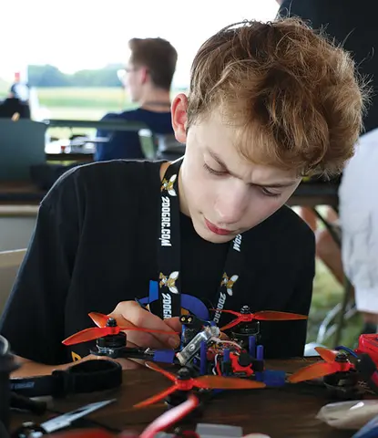 Boy focused on assembling a drone at an outdoor event.